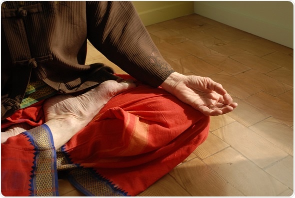 Cropped close up of mature female in yoga Lotus pose indoors. Image Copyright: Elena Ray / Shutterstock