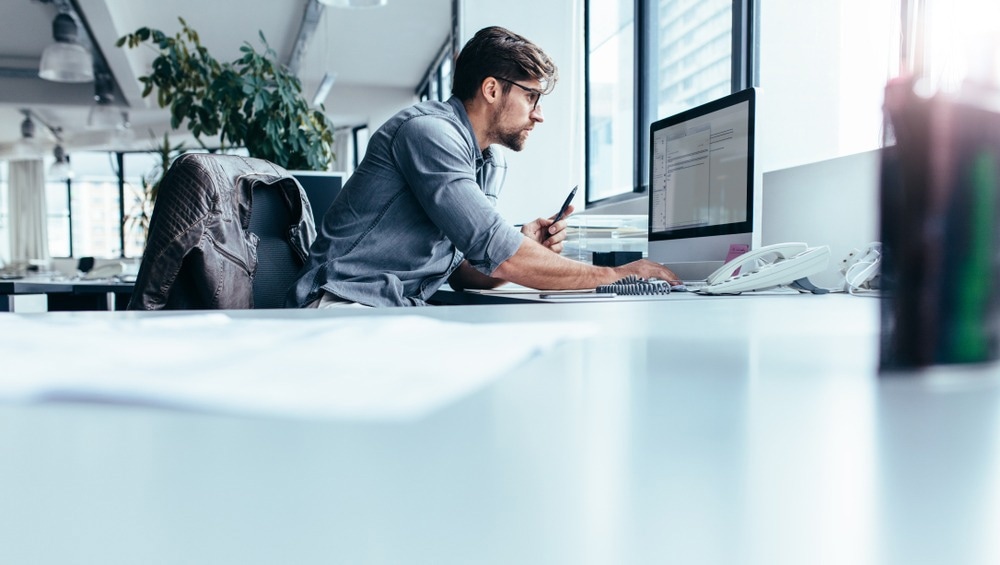 Young man sitting in office and working on desktop pc. Image Credit: Jacob Lund/Shutterstock.com