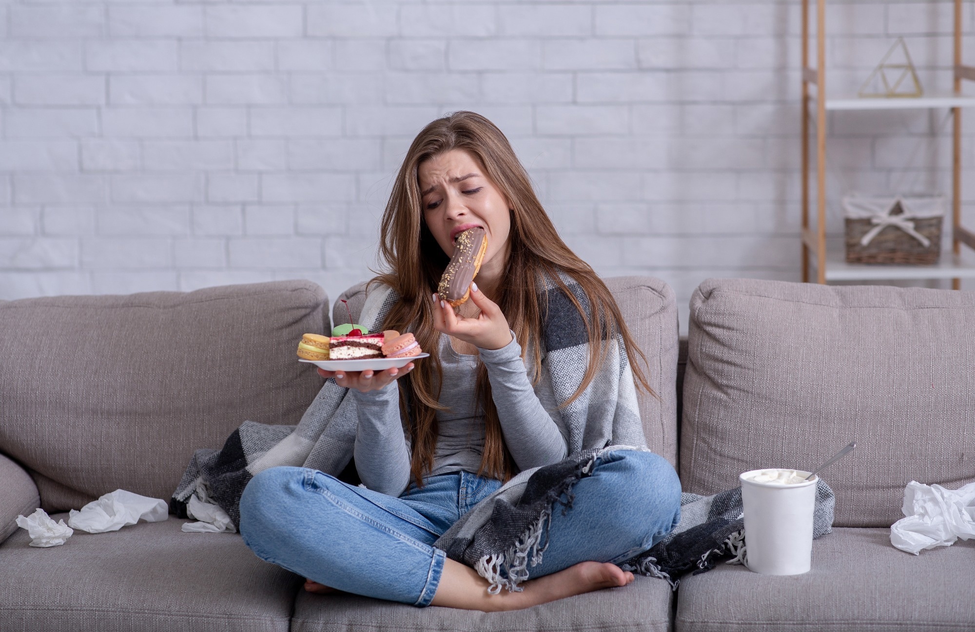 Frustrated young lady devouring pastry on sofa at home.
