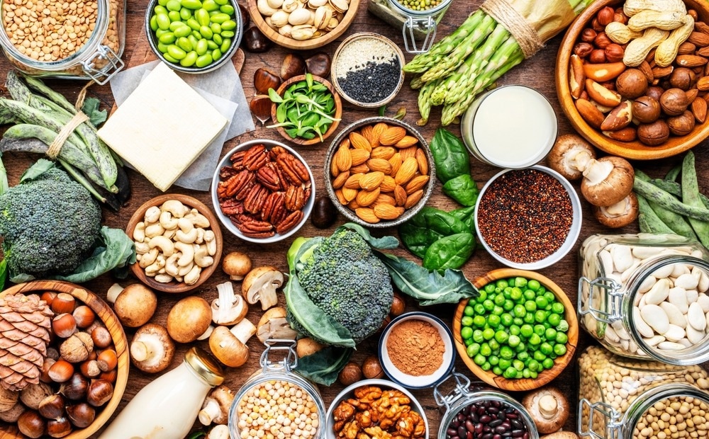A vibrant assortment of plant-based foods, including fresh vegetables, nuts, seeds, legumes, and grains, displayed on a wooden table, highlighting diverse and healthy dietary options.