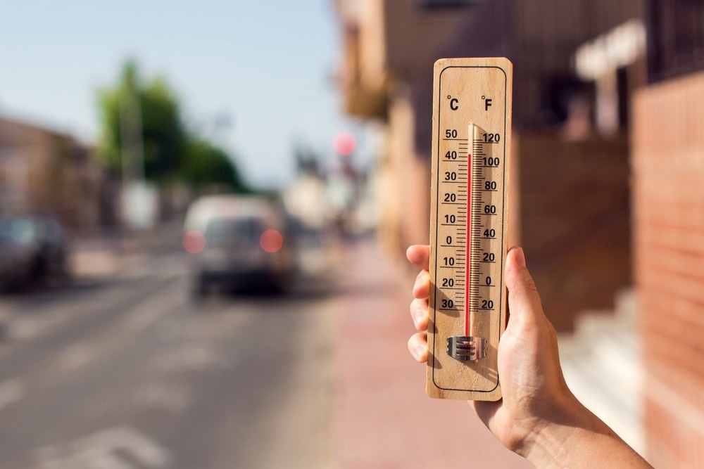 Thermometer in hand in front of an urban scene during heatwave.