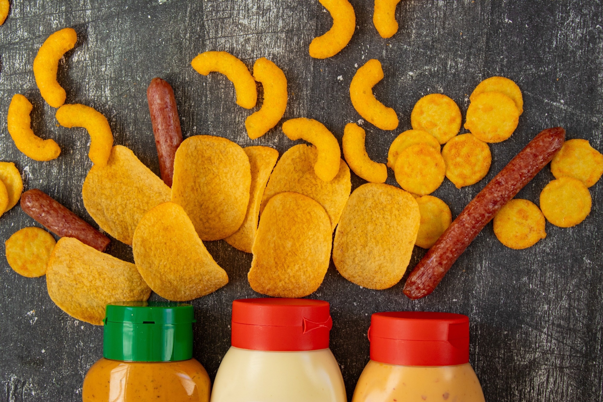 Fast food, unhealthy snacks, chips, sausages, and harmful sauces on a black background.