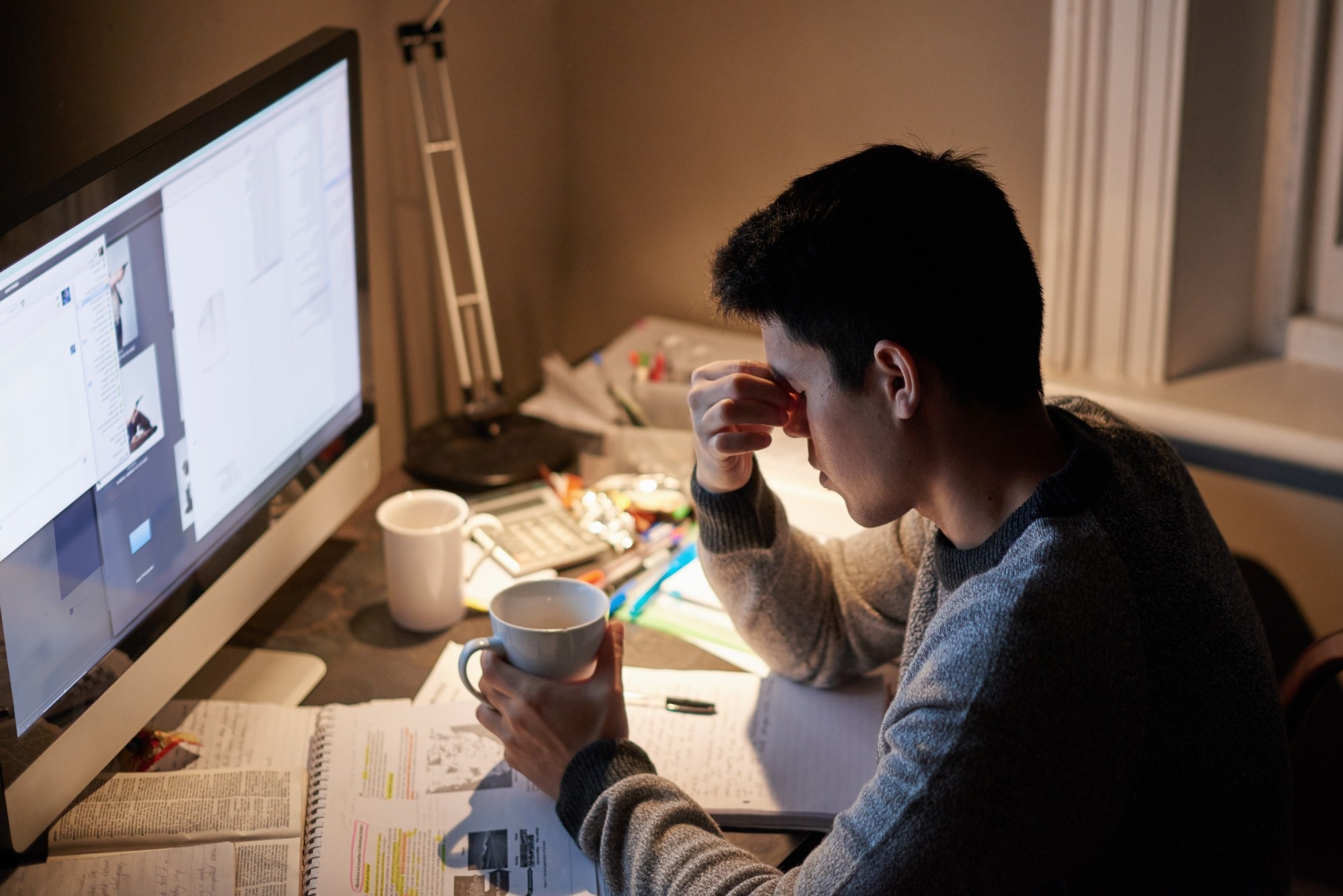 Man, studying and headache in night by computer for test, with coffee cup in his hand
