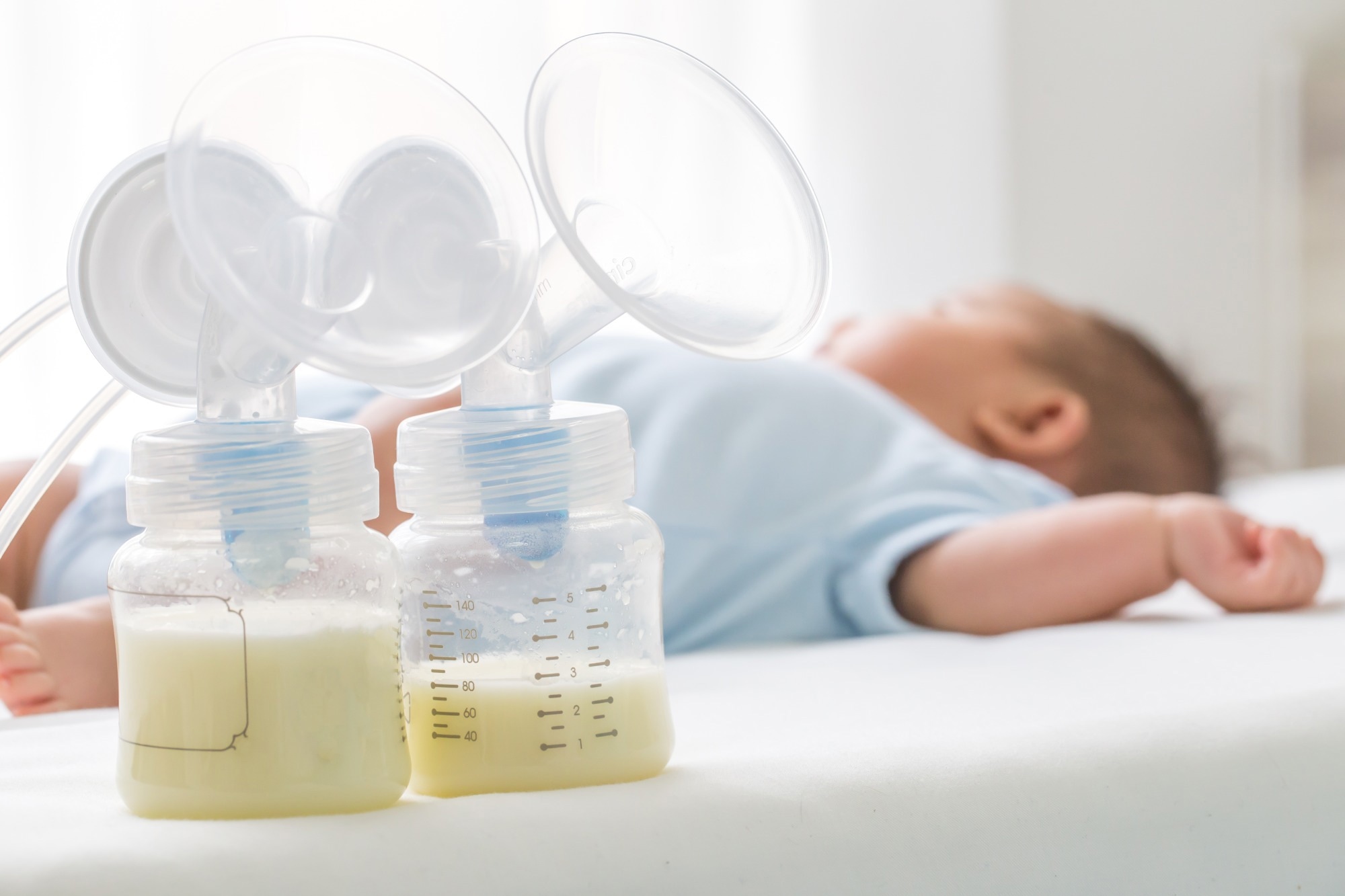 Breast milk pump and baby lying on the white bed