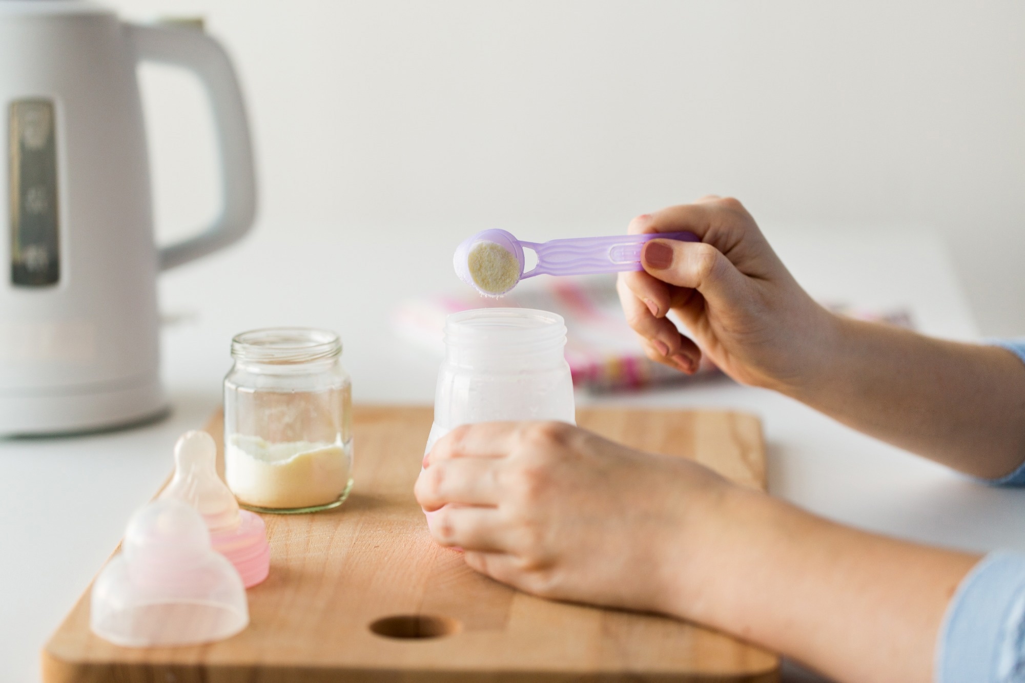 Mother hands with baby bottle and scoop preparing infant formula milk