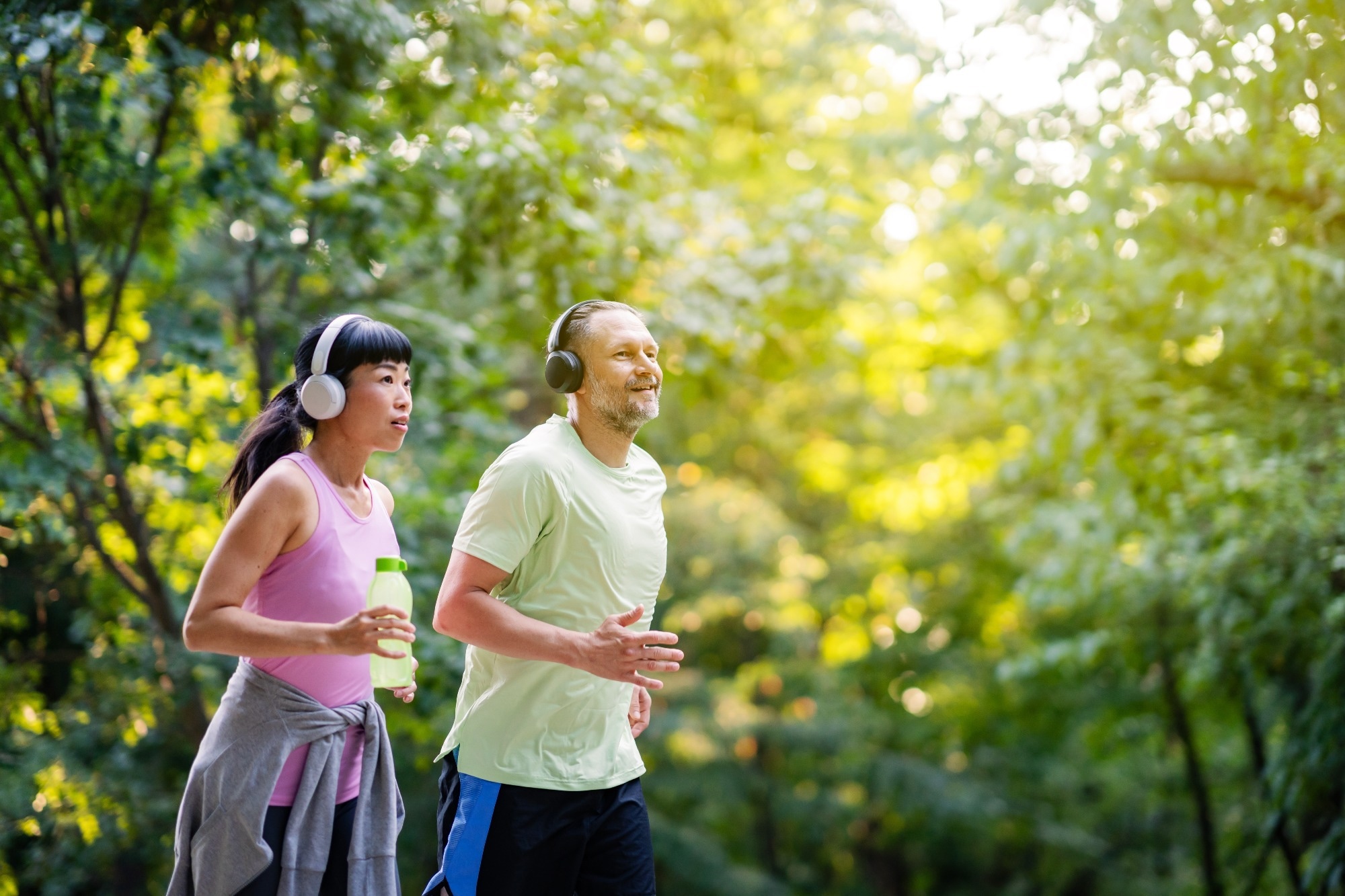 Happy diverse middle-aged couple jogging in forest, listening to music on headphones