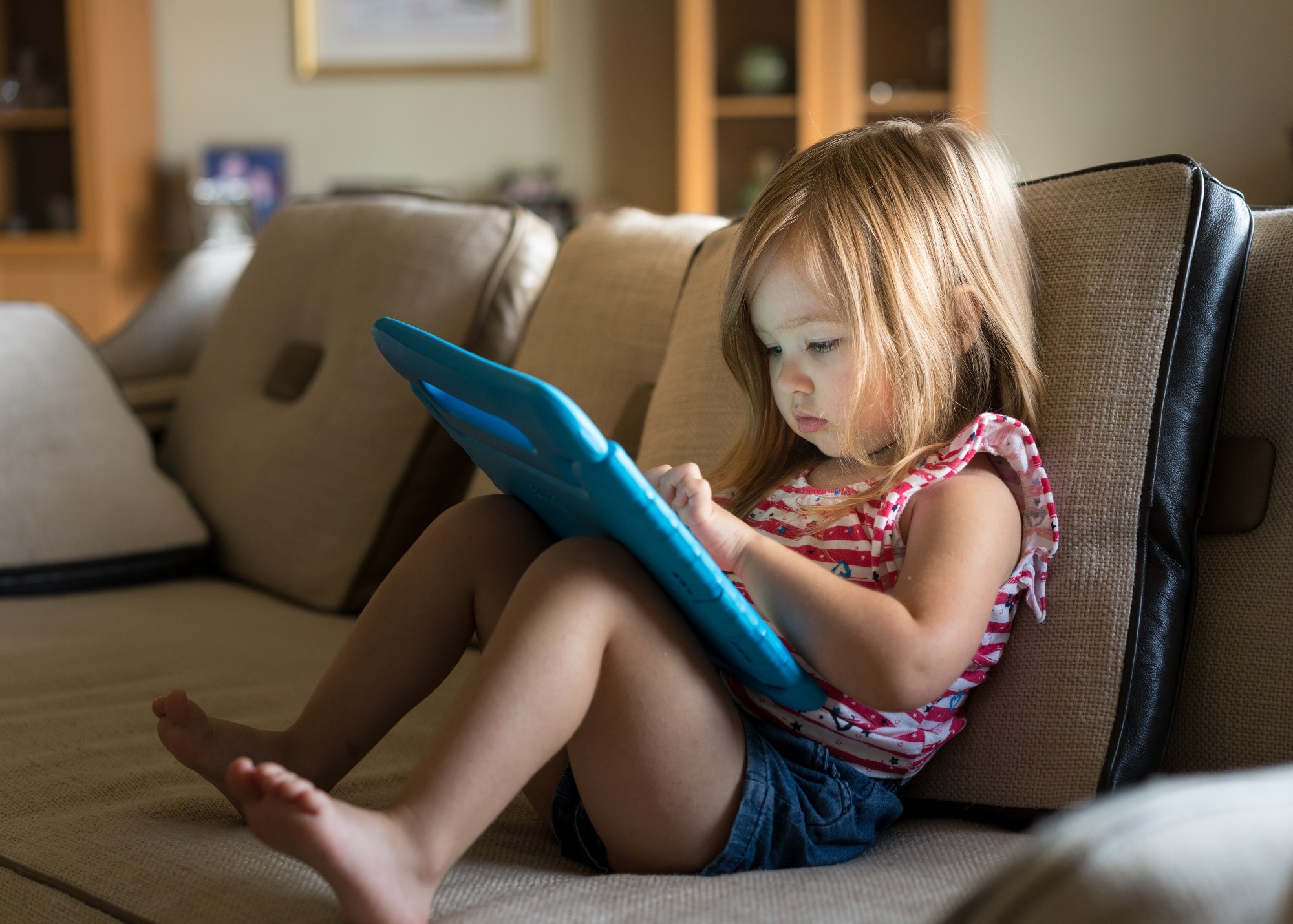 Young girl sitting at home on settee and using a child
